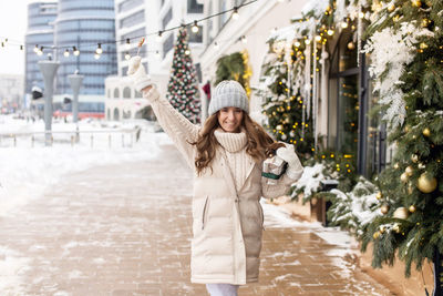 A happy girl walks around the city in winter with a colorful round lollipop and a gift box
