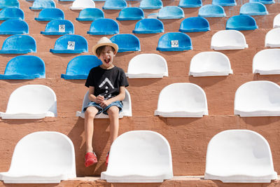 Boy in summer clothes sitting on one of chair on stadium and shout out with close eyes