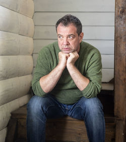 Thoughtful mature man with hands on chin looking away while sitting at home
