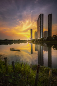 Scenic view of lake by buildings against sky during sunset