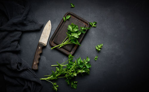 Green sprigs of parsley on a wooden cutting board and a knife. top view of black kitchen table
