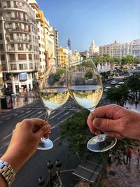 Cropped image of hand holding wine glass against buildings in city