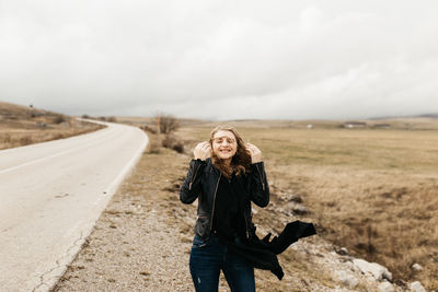 Full length of smiling young woman standing on land against sky