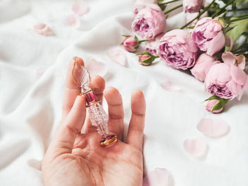 Woman holds pink glass bottle for perfume with eastern ornament. rose bouquet,petals as decoration.