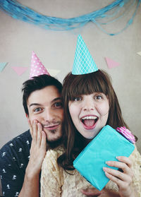 Portrait of smiling friends wearing party hat against wall at home