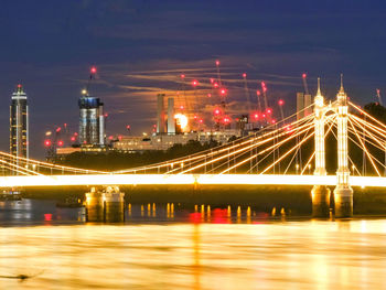 Illuminated bridge over river against sky in city at night