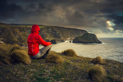 Rear view of woman sitting on mountain by sea