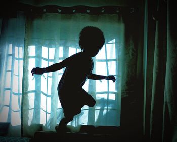 Side view of silhouette boy standing against window at home
