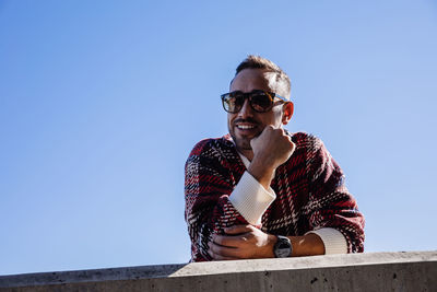 Low angle view of young man wearing sunglasses against clear sky