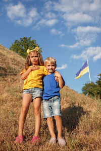 Girl in yellow and boy in blue near biggest national flag of ukraine. pray for peace and victory