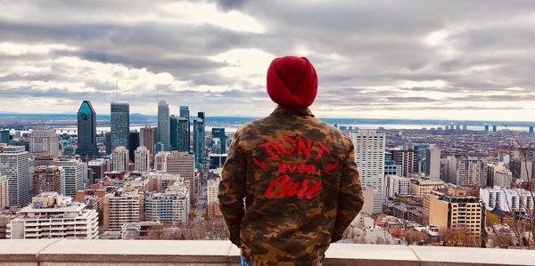 Rear view of man looking at city buildings against sky