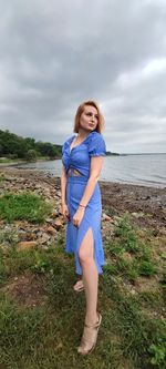 Young woman standing on field by sea against sky