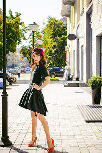 Beautiful young woman in black dress standing on sidewalk in city