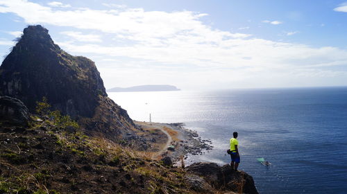 Man on rock by sea against sky