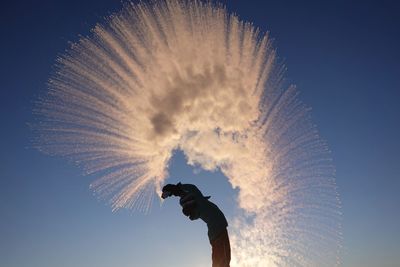 Woman throwing snow against clear blue sky