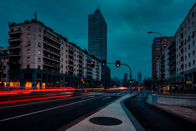 Light trails on city street by buildings against sky at dusk milan italy 