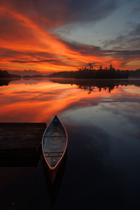 Fiery sunrise on a calm lake with canoe