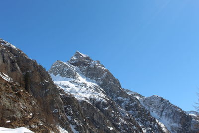 Low angle view of snow covered mountains against blue sky