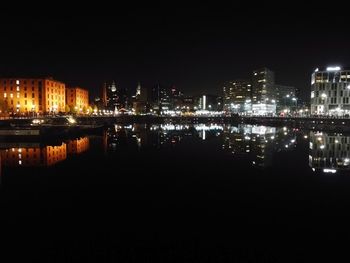Illuminated buildings by river against clear sky at night