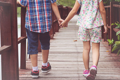 Low section of siblings holding hands while walking on footbridge