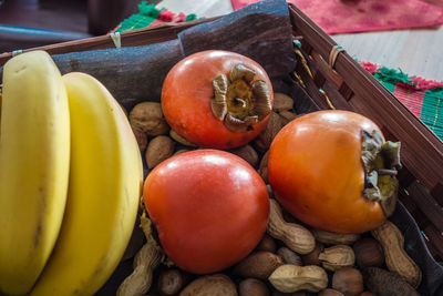 Close-up of persimmons with peanuts and bananas in basket