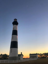 Low angle view of lighthouse by building against sky during sunset