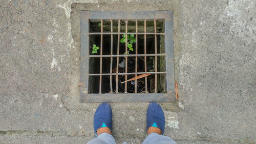 Low section of person standing on street by sewer