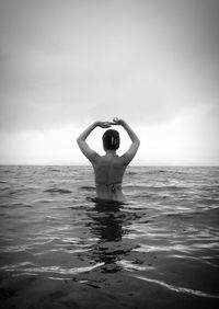 Rear view of woman with arms raised standing in sea against sky