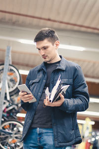 A young man with a phone and goods in his hands stands in the store.