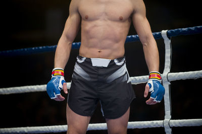 Midsection of shirtless boxer standing in boxing ring