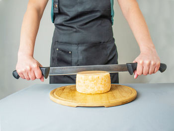 Two-handed cheese knife, cheese knife, worker slicing the cheese, close up of cutting cheese
