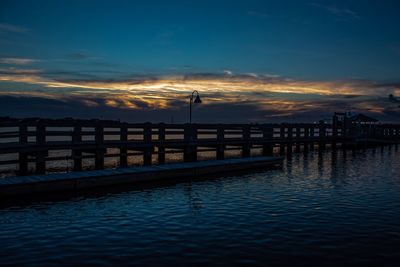 Pier over river against sky during sunset