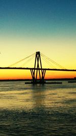 Silhouette suspension bridge over sea against clear sky during sunset