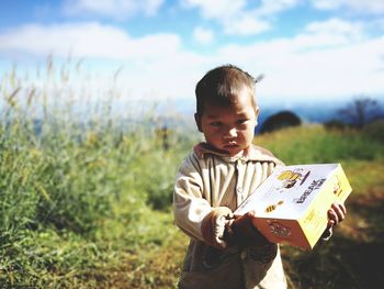 Portrait of cute boy holding box on field