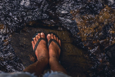 Low section of man standing amidst stream on rock