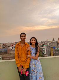 Portrait of smiling young man and woman standing against sky during sunset