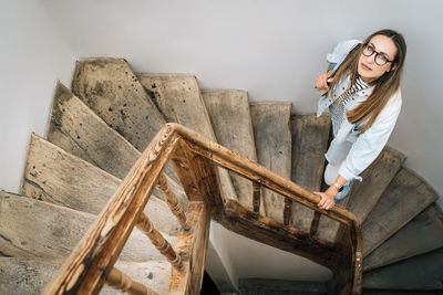 A woman looks up standing on an old wooden staircase