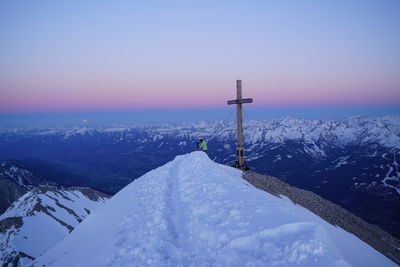 Man standing on snow covered mountain by cross against sky during winter