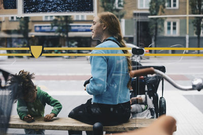 Mother and children sitting on bench at bus stop in city