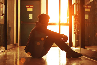Side view of silhouette young man sitting on floor in corridor