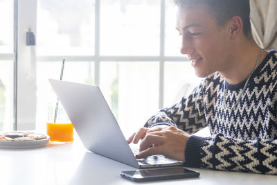 Smiling teenager boy using laptop at home