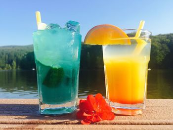 Close-up of drinks in glasses on table by lake