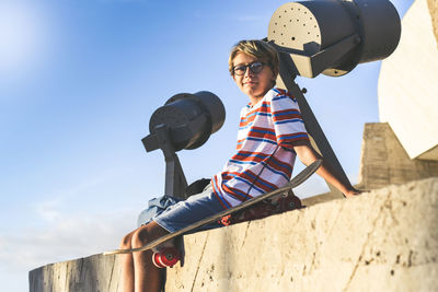 Portrait of boy sitting on wall against sky