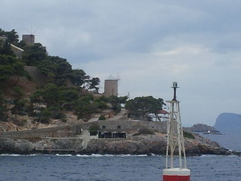 Lighthouse in front of sea against cloudy sky