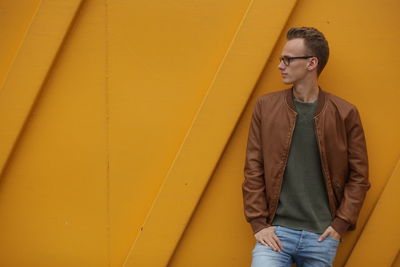 Close-up of young man standing against yellow wall