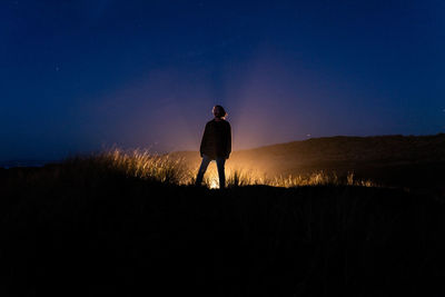 Rear view of man standing on field against sky at night