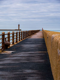 Wooden posts on footpath by sea against sky