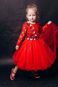 Cute girl in red dress posing against black background