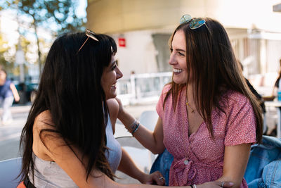 Happy female friends talking while sitting at outdoor cafe in city