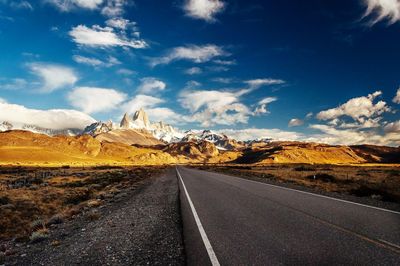 Road leading towards rocky mountains against sky